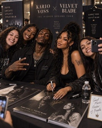 Kario Voss and Velvet Blade at a signing table with fans, posters of the two of them on the table